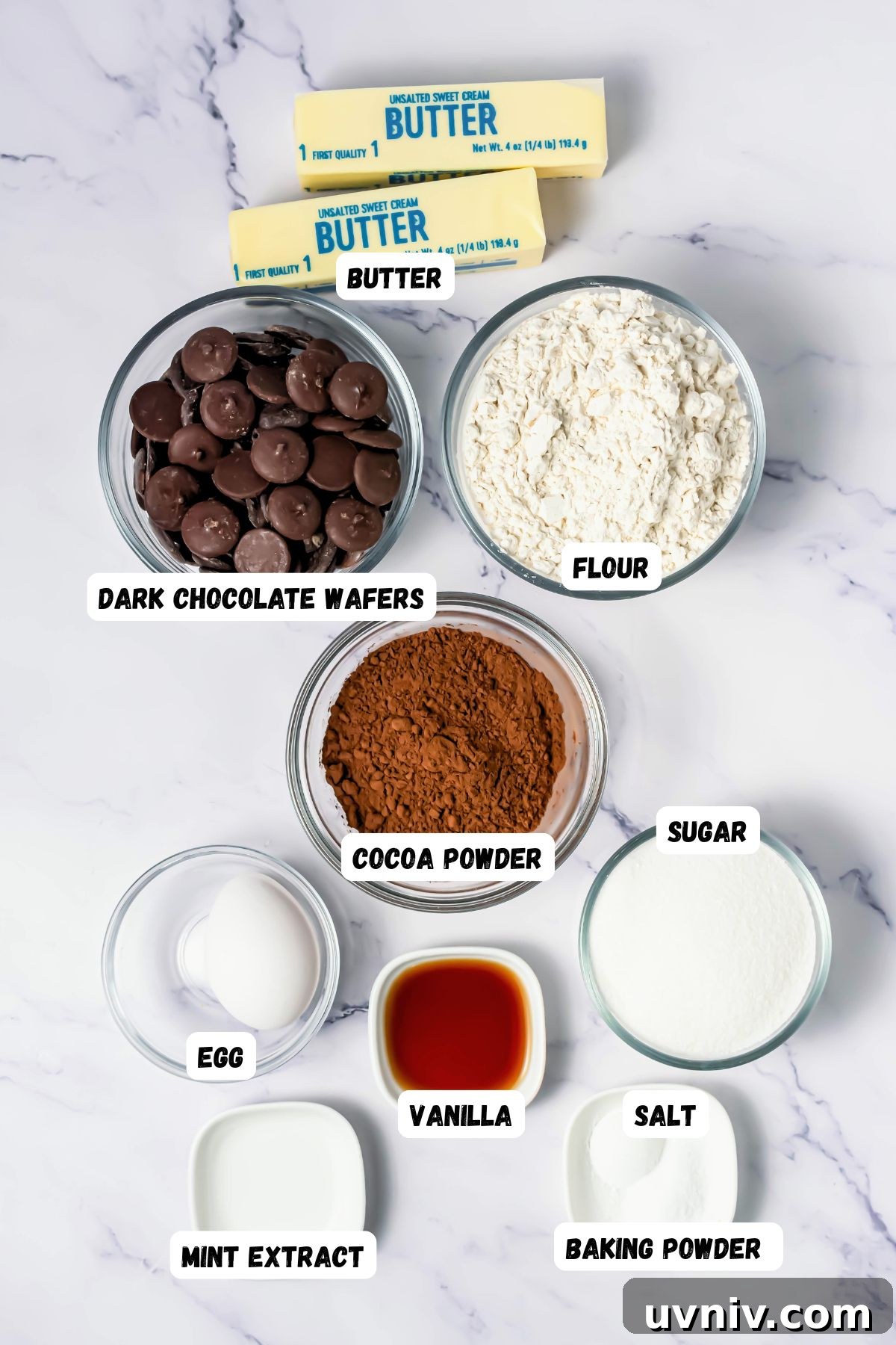 Ingredients like flour, sugar, butter, and more, measured into small bowls on a white marble table.