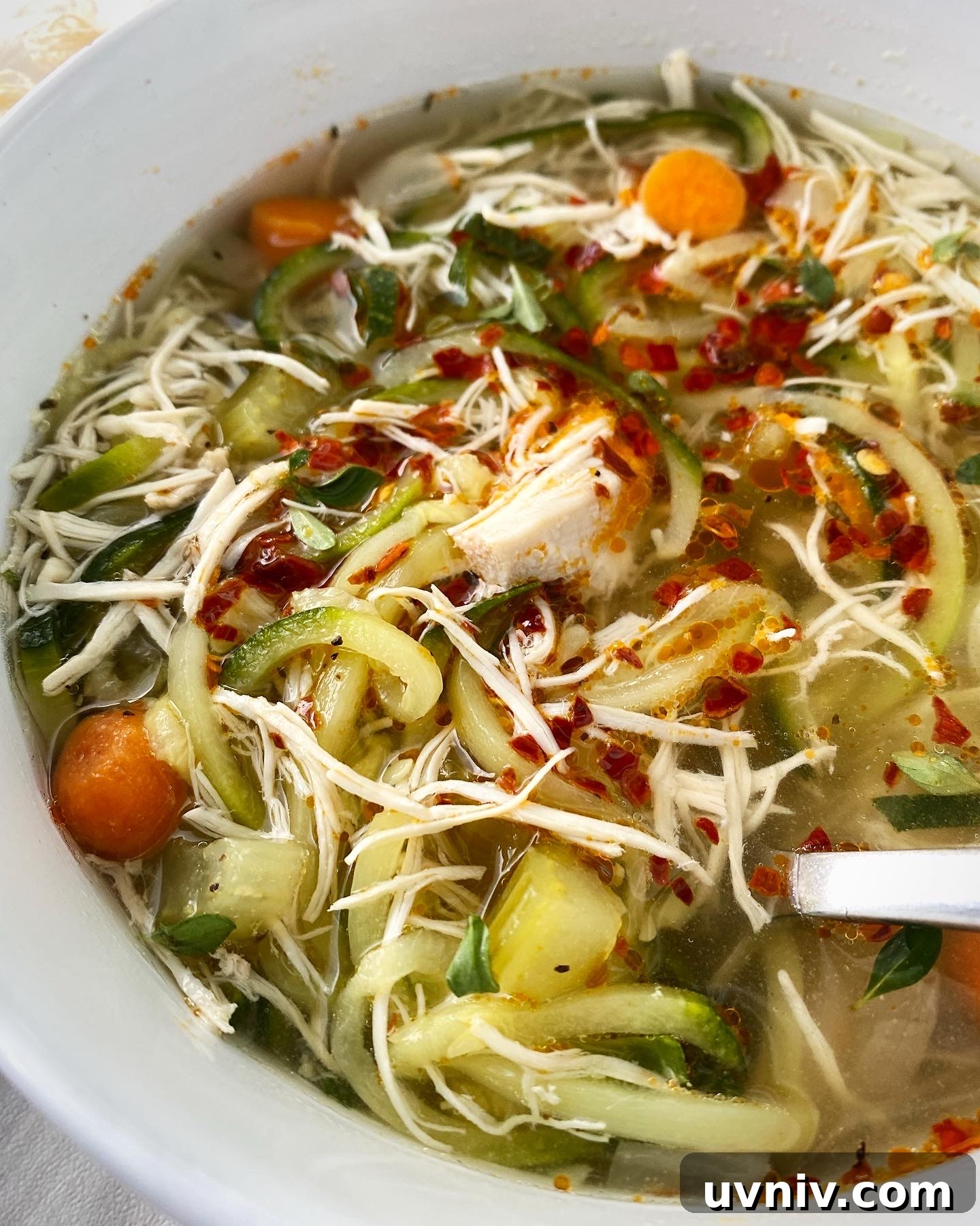 close up, side view shot of slow cooker chicken zoodle soup in a white bowl garnished with chili oil