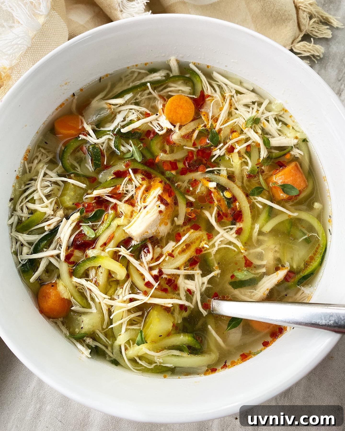 overhead shot of slow cooker chicken zoodle soup in a white bowl garnished with chili oil
