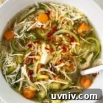 overhead shot of slow cooker chicken zoodle soup in a white bowl garnished with chili oil