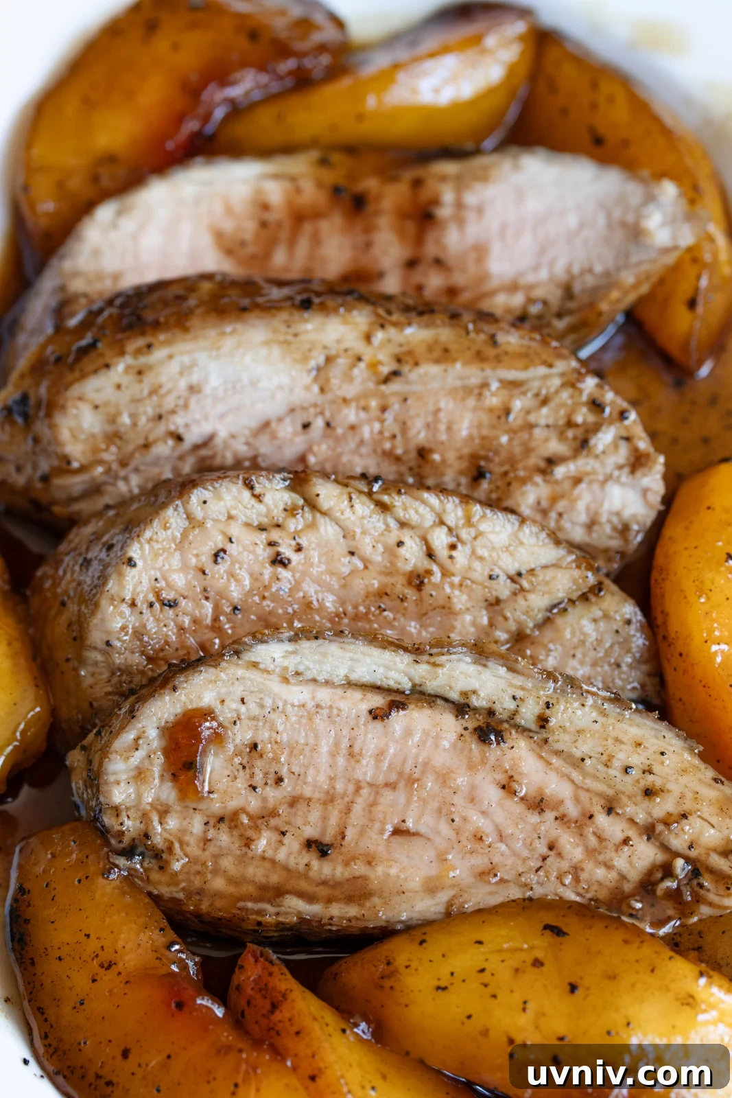 Sliced glazed pork tenderloin surrounded by peaches served on a white dish