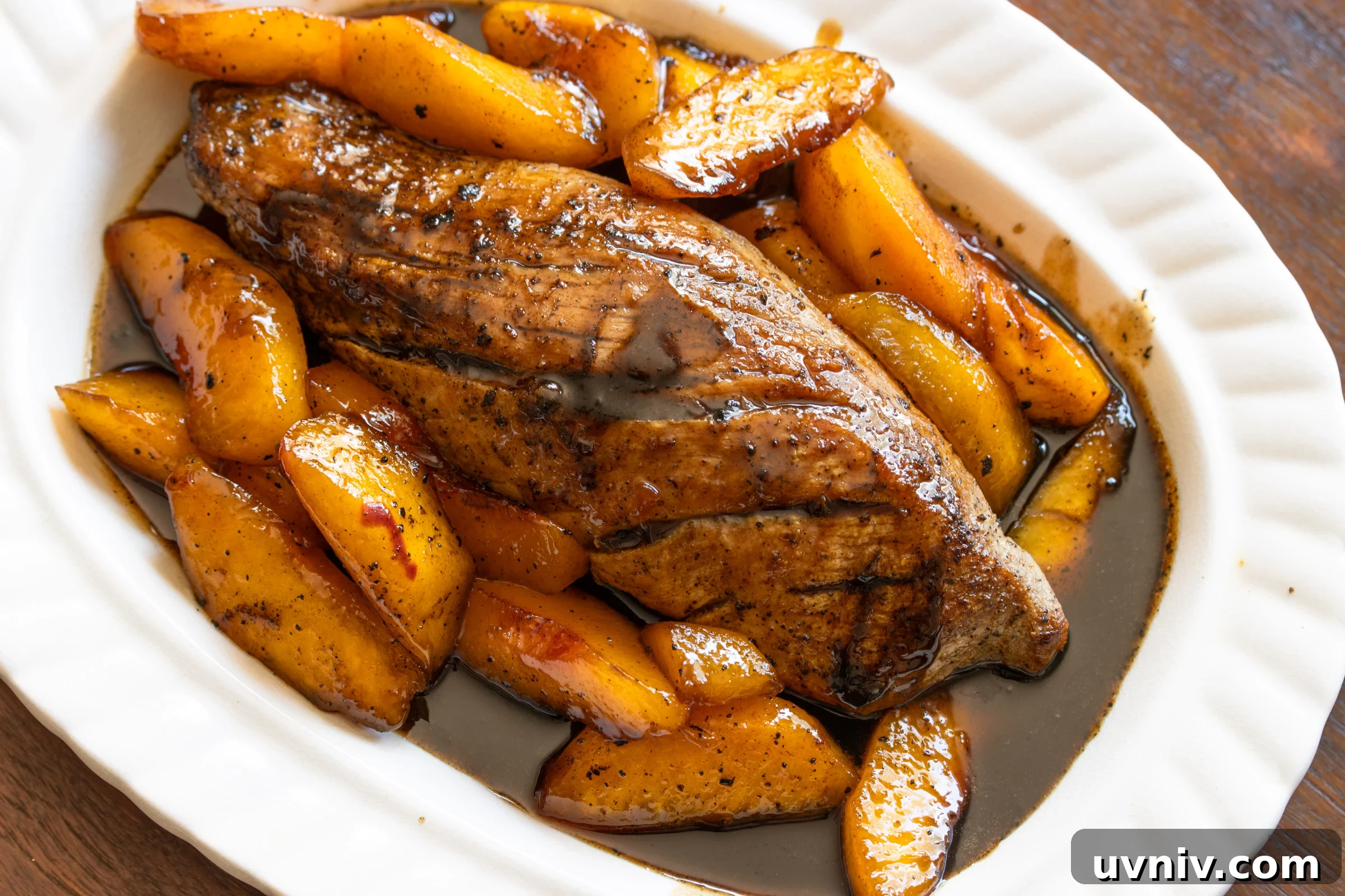 Pork tenderloin with peach glaze surround it in a white scalloped serving dish.