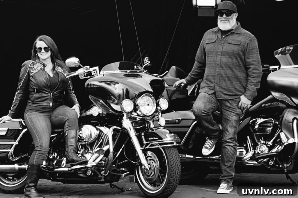 A black and white photo of Dustin and Brenda Taylor standing next to their motorcycles.