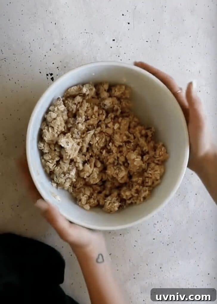 Hands holding a white bowl of crumble.