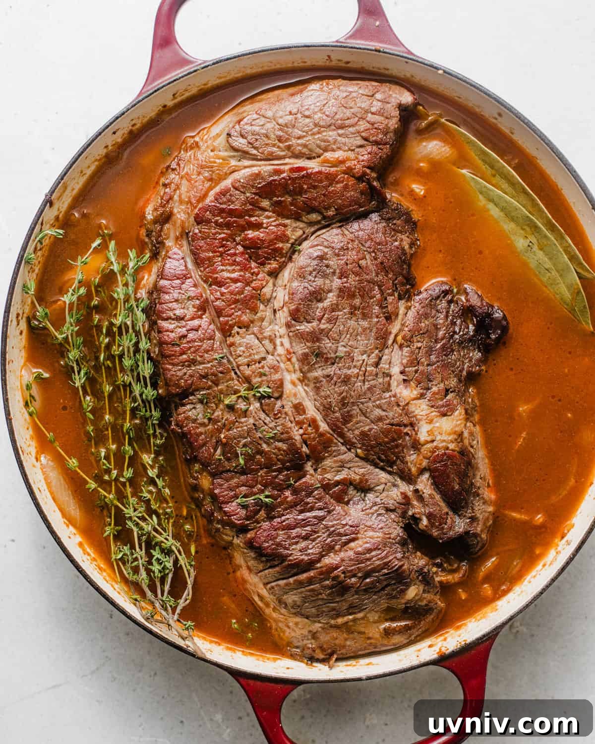 chuck roast in the pot with thyme, caramelized onions, whiskey, red wine, and bay leaves. 