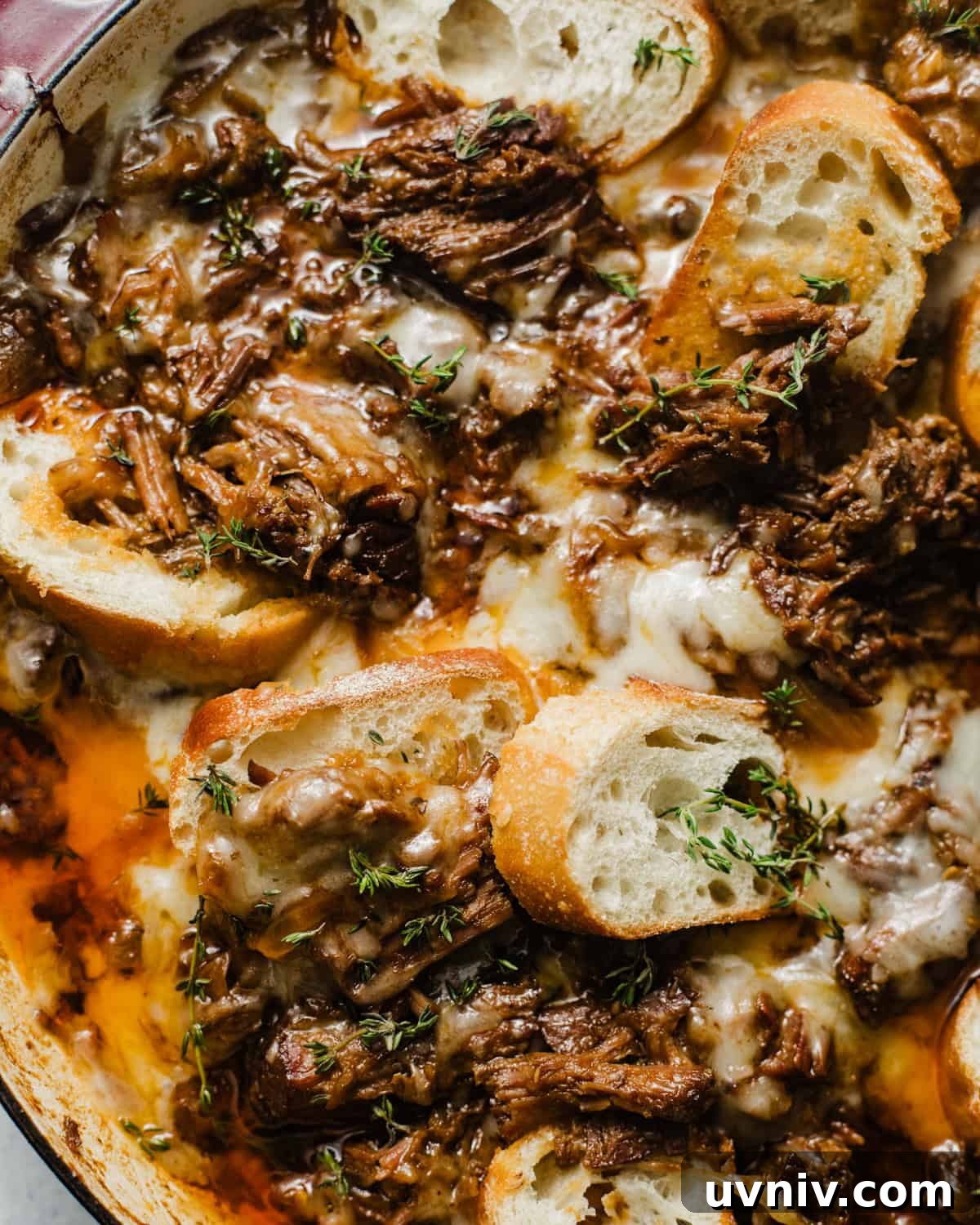 up close photo of french onion pot roast in a braising pan topped with gruyere cheese and sliced baguettes.