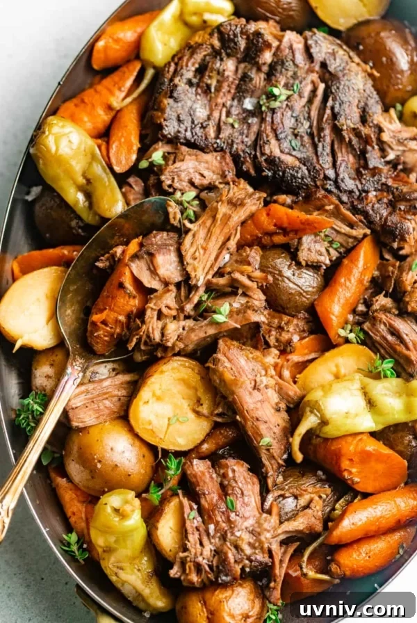 mississippi pot roast in a serving dish with a spoon and garnished with fresh thyme and pepperoncini peppers.