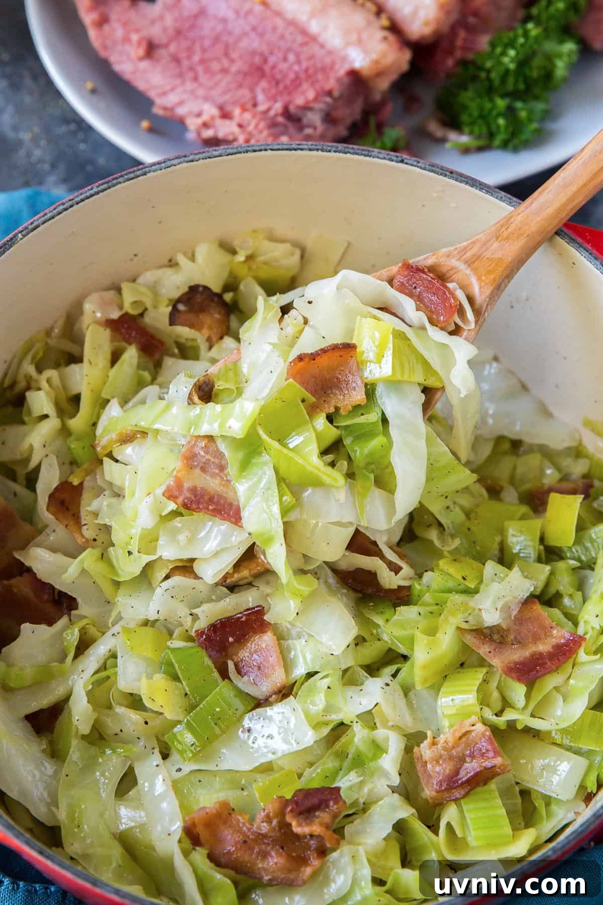 A wooden spoon scooping sauteed leeks from a Dutch oven.