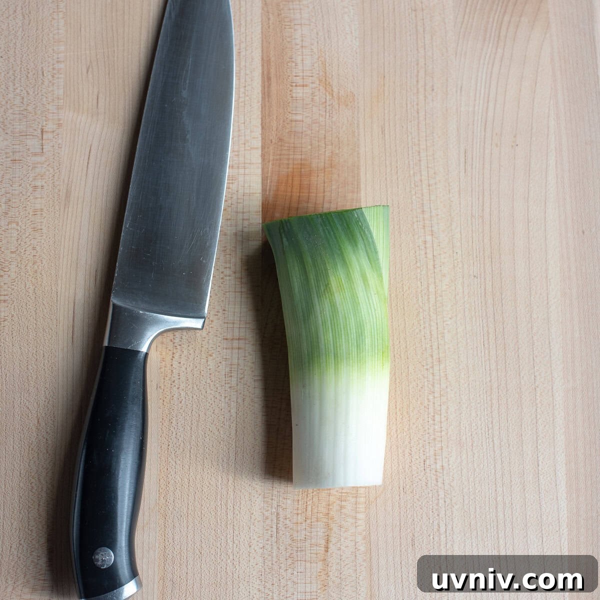 A trimmed leek on a cutting board with a knife.